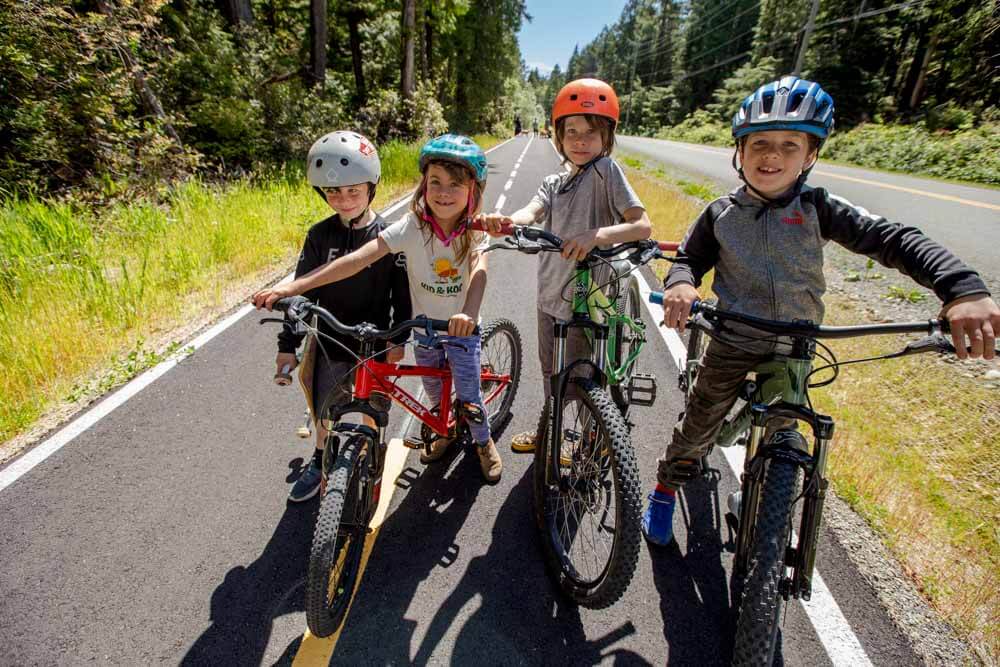 Four kids on bikes with helmets pose for camera