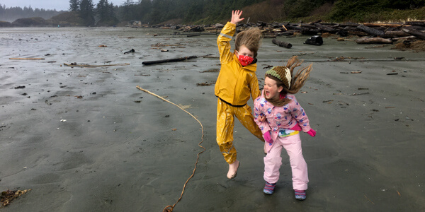 Two kids in rain suits jumping on beach