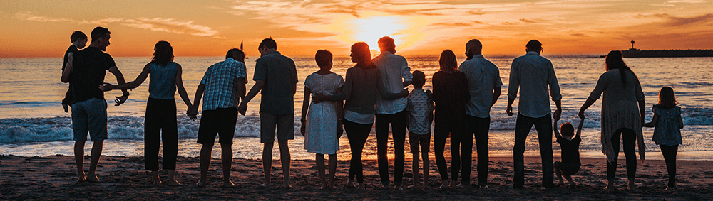 Group of people holding hands on beach at sunset